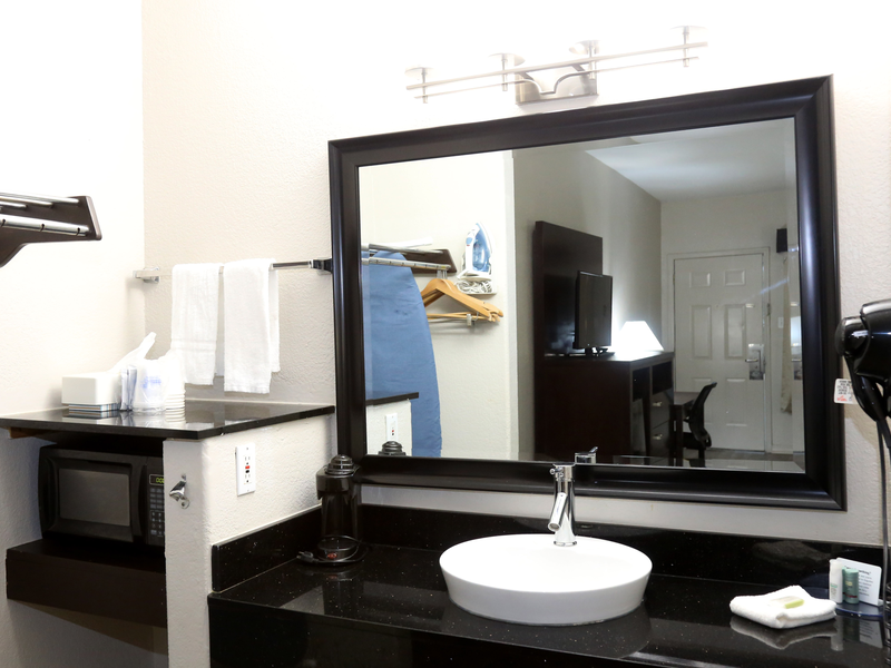 Guest room vanity with sink, mirror, microwave, and ironing area